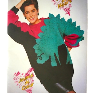 May include: A knitting pattern booklet from Patons called "Young at Heart" featuring a woman wearing a black, pink, and teal sweater with a dinosaur design. The booklet also includes the French translation "Jeunes de Coeur".