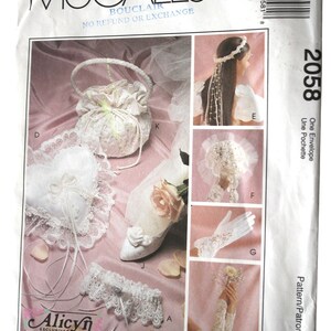 May include: McCall's bridal pattern envelope featuring various wedding accessories. Includes a heart-shaped ring pillow, a beaded handle purse, a garter, a shoe, a headpiece, gloves, and a pattern for long sleeves. The price is $13.95.