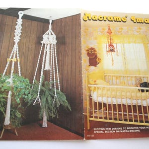Peut inclure: Un livre ouvert présentant des créations en macramé. La page de gauche montre deux suspensions de plantes en macramé blanc avec des plantes vertes. La page de droite affiche un berceau et d'autres décorations en macramé. Le texte dit "Macrame Images".