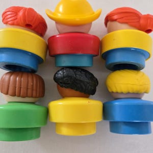 May include: A selection of vintage Fisher-Price Little People figures. The figures have different hair colours, including red, brown, black, and yellow. The figures have yellow, red, blue, and green clothing. The figures are stacked together.