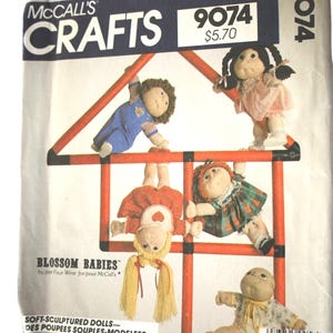 May include: McCall's Crafts pattern 9074 for Blossom Babies soft-sculptured dolls. The packaging features five dolls with yarn hair and fabric clothing, shown climbing on a red frame. Text includes the pattern number, price, and title.