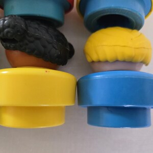 May include: Close-up of colourful plastic toy figures. The figures have yellow, blue, and brown bases with different coloured heads, including yellow and black hair. The toys are likely designed for children.