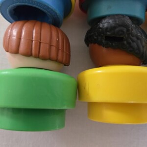 May include: Close-up of several vintage toy figures. The figures have brown, black, and yellow hair, with green and yellow bases. The figures are stacked on top of each other, with blue and red tops.