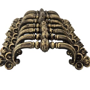 Peut inclure: Un ensemble de huit poignées de cabinet en laiton antique avec des motifs ornés et enroulés. Les poignées sont disposées en demi-cercle, mettant en valeur leurs détails complexes.