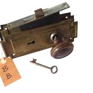 May include: Antique brass door lock with a brown wooden knob, a key, and a brown tag with the letters "BB" written on it.