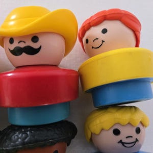 May include: Close-up of several vintage Fisher-Price Little People figures. One figure wears a yellow cowboy hat and has a black moustache. Other figures have red, yellow, and blonde hair. The figures have red, blue, and yellow clothing.