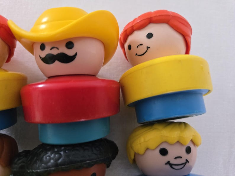 May include: Close-up of several vintage Fisher-Price Little People figures. One figure wears a yellow cowboy hat and has a black moustache. Other figures have red, yellow, and blonde hair. The figures have red, blue, and yellow clothing.