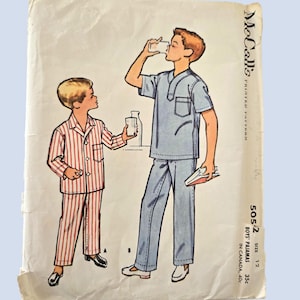 May include: Vintage McCall's sewing pattern for boys' pyjamas. The illustration shows two boys, one in striped pyjamas and the other in a blue pyjama set. The pattern cover shows signs of age and wear.