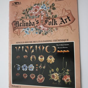 May include: A book titled "Melinda's Folk Art" with a single brush multi-loading technique. The cover features a floral design with pink, red, and white roses, blue flowers, and green leaves. The book is volume 1 and includes 13 basic strokes and rococo flowers.