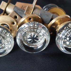 May include: Three clear glass door knobs with a decorative pattern. The knobs are mounted on brass plates.