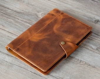 May include: A brown leather bound journal with a brass button closure. The journal has a distressed look and is closed.