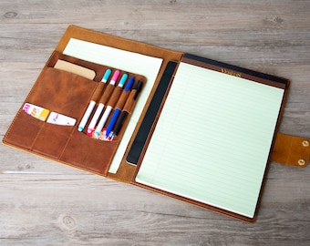 May include: A brown leather portfolio with a notepad, pen holders, and card slots. The notepad has lined paper and the text "NOTES" at the top.