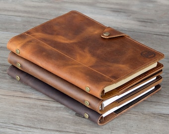 May include: Three brown leather journals stacked on top of each other. The top journal has a flap closure with a brass button. The top journal also has a brass logo on the front cover.