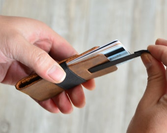 May include: A brown leather wallet with a black elastic band and a metal clip. The wallet is open and has several cards inside.