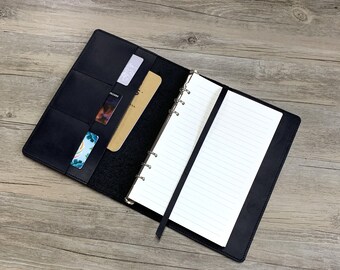 May include: Black leather bound notebook with a built-in card holder and a ribbon bookmark. The notebook has a six-ring binder system and lined pages.