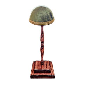 May include: A hat stand with a green velvet hat. The hat has a gold trim. The stand is made of wood with a dark brown finish. The base is square and the stem is turned.