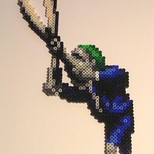 May include: A pixel art figure made of colourful beads, depicting a person holding a pair of scissors. The figure is wearing a blue and black suit with a green hat.