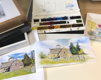 May include: Two watercolor paintings of a stone church with a tower, surrounded by trees and a graveyard. The paintings are on white paper and are next to a palette of watercolors.