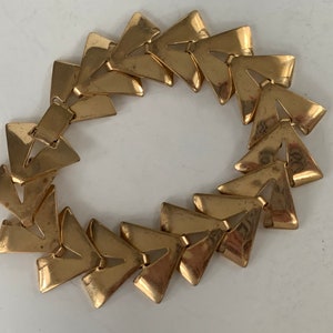 May include: A gold-toned bracelet made of interlocking triangular links. The bracelet is a circle and is made of metal.