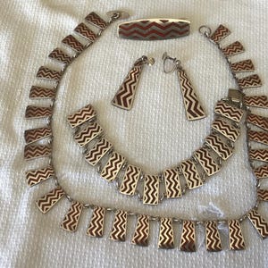 May include: A set of silver jewelry with a zig-zag pattern in red and white enamel. The set includes a necklace, a bracelet, a brooch, and a pair of earrings.