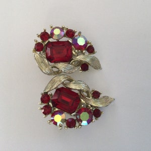 May include: A pair of vintage clip-on earrings with a silver tone metal setting and red and iridescent rhinestones.