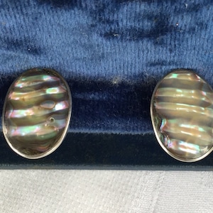 May include: A pair of oval-shaped cufflinks with iridescent mother-of-pearl inlays. The inlays have a striped pattern and are set in silver.