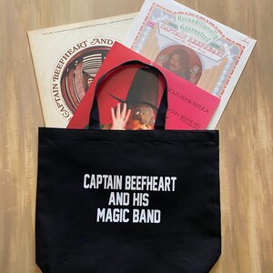 May include: Black tote bag with the text "CAPTAIN BEEFHEART AND HIS MAGIC BAND" in white. The bag contains three vinyl records with album art. The records are in various colors, including red, beige, and white.