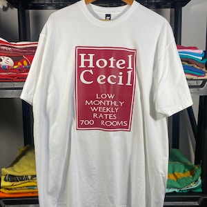 May include: White t-shirt with a red rectangle graphic that says "Hotel Cecil" with the text "Low Monthly Weekly Rates 700 Rooms" underneath.