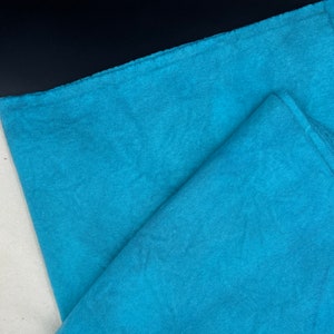May include: A folded piece of teal blue fabric with a slightly textured surface.