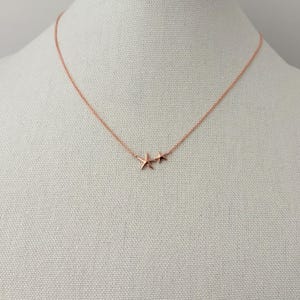 May include: A rose gold necklace featuring a delicate chain and two small starfish charms of different sizes positioned together. The metal has a smooth, polished finish, and the starfish pendants are attached directly to the thin, circular link chain.