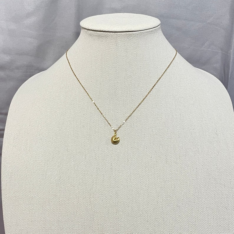 May include: A gold chain necklace with a small gold fortune cookie pendant.