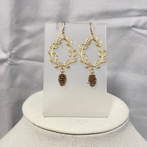 May include: Gold tone earrings with a wreath design and a pine cone dangle.