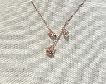 Peut inclure: Un collier en or rose avec un pendentif délicat en forme de rose. La rose est détaillée avec des feuilles et une tige.