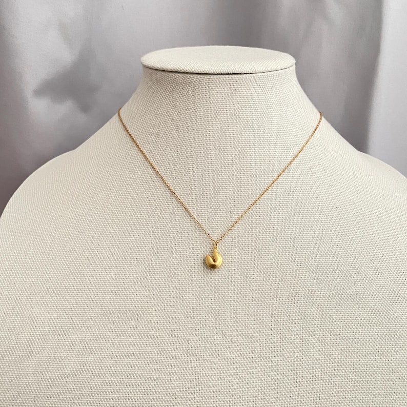 May include: A gold chain necklace with a small, round pendant. The pendant is shaped like a fortune cookie.