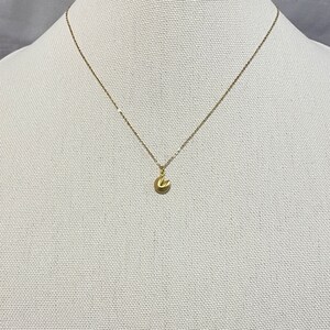 May include: A gold chain necklace with a small gold charm in the shape of a fortune cookie.