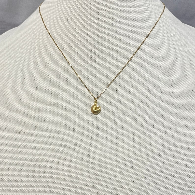 May include: A gold chain necklace with a small gold charm in the shape of a fortune cookie.