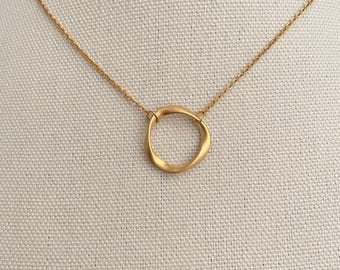 Puede incluir: Un collar de cadena dorada con un colgante simple de círculo retorcido.