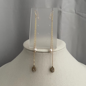 May include: A pair of gold chain earrings with a small pearl and a gold acorn charm on each earring.