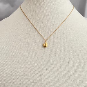 May include: A gold chain necklace with a small, gold, abstract pendant. The pendant is shaped like a crescent moon.