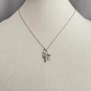 May include: A silver-toned necklace featuring a floral pendant with a small pearl accent. The pendant is a detailed, five-petal flower design. The necklace is displayed on a neutral-colored mannequin.