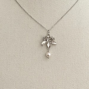 May include: A silver necklace featuring a dainty flower pendant with a single pearl drop.