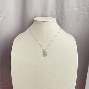 May include: A silver necklace with a flower pendant. The pendant is a detailed, three-dimensional flower design. The necklace is displayed on a white mannequin against a neutral background.