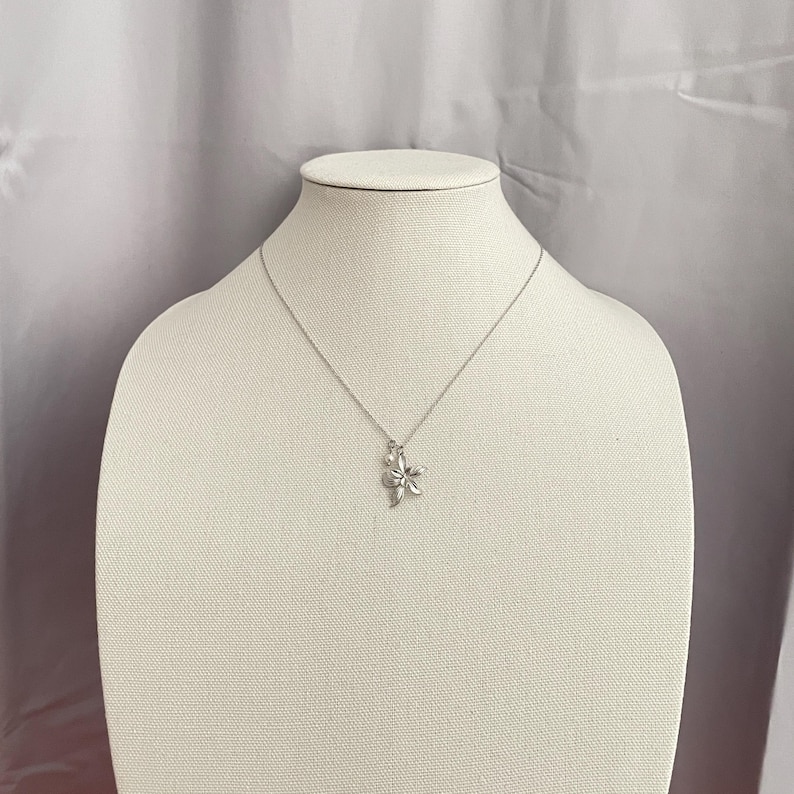 May include: A silver necklace with a flower pendant. The pendant is a detailed, three-dimensional flower design. The necklace is displayed on a white mannequin against a neutral background.