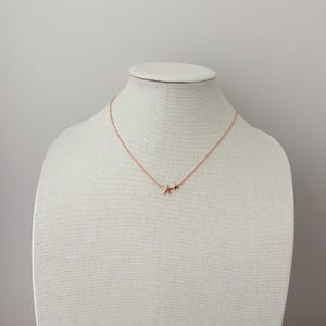 May include: A rose gold necklace featuring a delicate chain and two small, five-pointed starfish charms positioned together at the center. The metal has a warm, metallic finish, and the design is simple, consisting of the chain and the starfish.