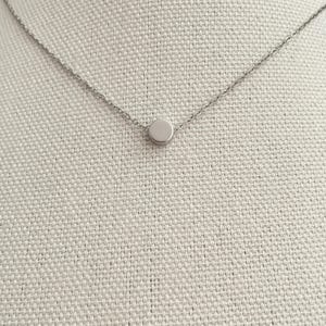 Könnte beinhalten: Eine silberne Kettenkette mit einem kleinen, runden Anhänger.