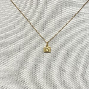 May include: A gold chain necklace with a small camera charm pendant.