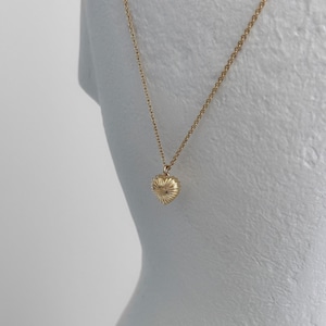 May include: A gold chain necklace with a heart-shaped pendant. The pendant has a textured, ribbed surface.