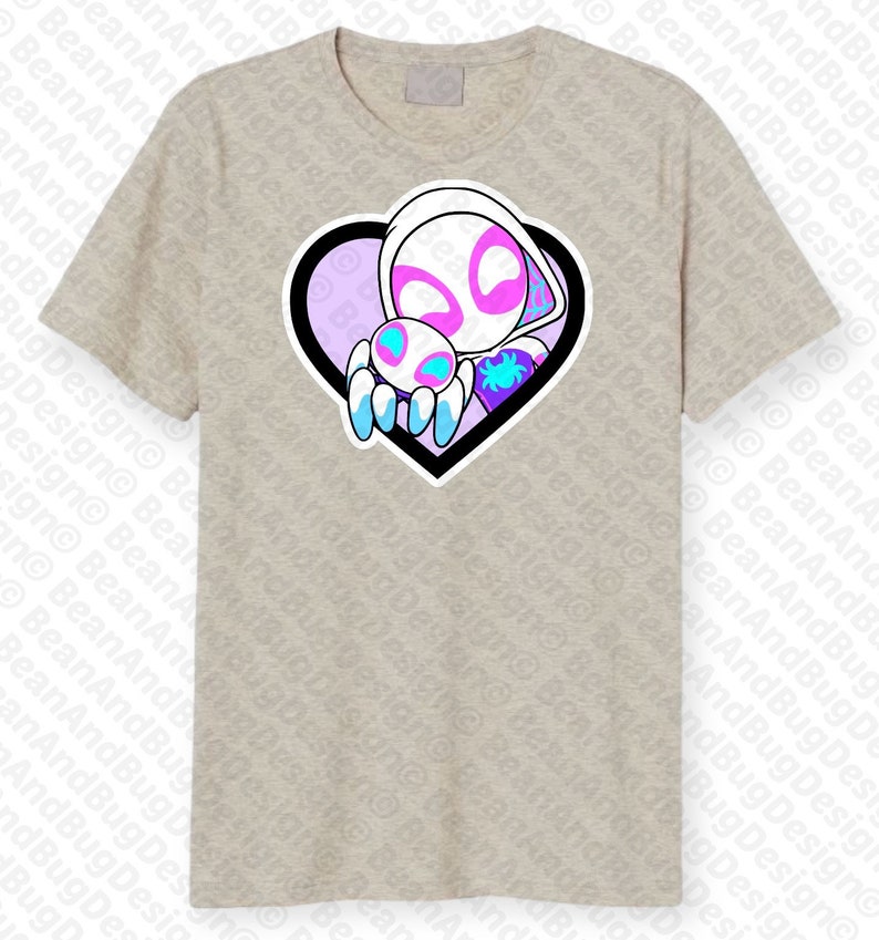 Op de afbeelding: Een lichtgrijs T-shirt met een afbeelding van een witte spinnenvrouw die een kleinere spin vasthoudt in een hartvormig frame. Het hart is zwart omrand en heeft een paarse en blauwe gradi&euml;nt aan de binnenkant.
