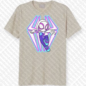 May include: A beige t-shirt with a graphic of a cartoon superhero in a white suit with purple and blue accents. The superhero is flying with a web design behind them.