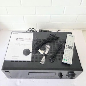 Puede incluir: Un receptor AV multicanal Sony negro con un mando a distancia, cables y un manual. El manual dice "Multi Channel AV Receiver". El receptor tiene un diseño elegante y moderno.